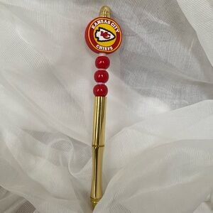 A golden pen with red tiny beads with white, tiny beads, and a Kansas City logo